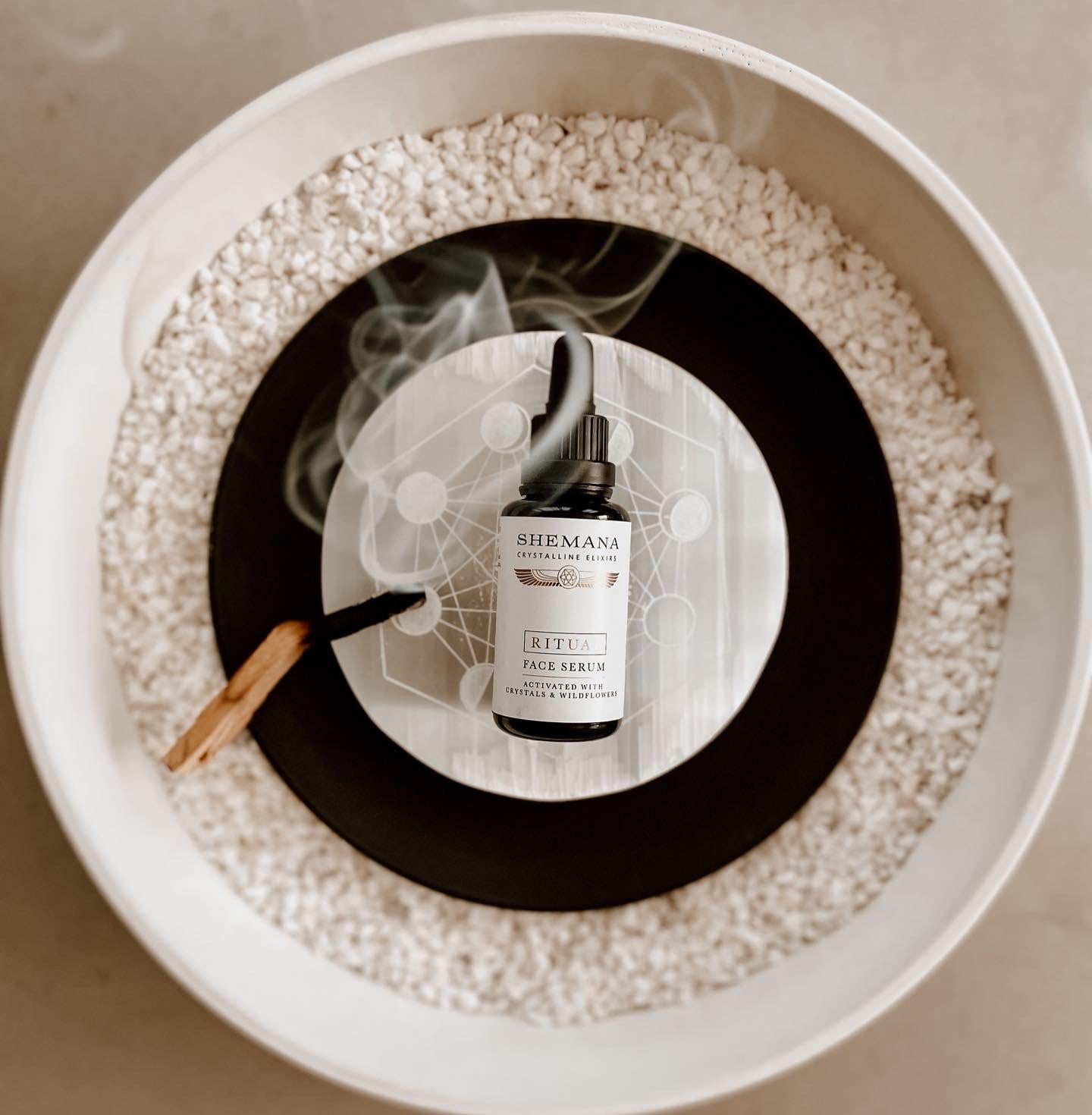 miron bottle of face serum. Shemana logo. palo santo smoke in a white bowl with coding white quartz
